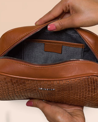 Close-up of the Benheart Afef Medium leather crossbody bag in Cuoio color, held open by a model to showcase interior compartments and detailing.