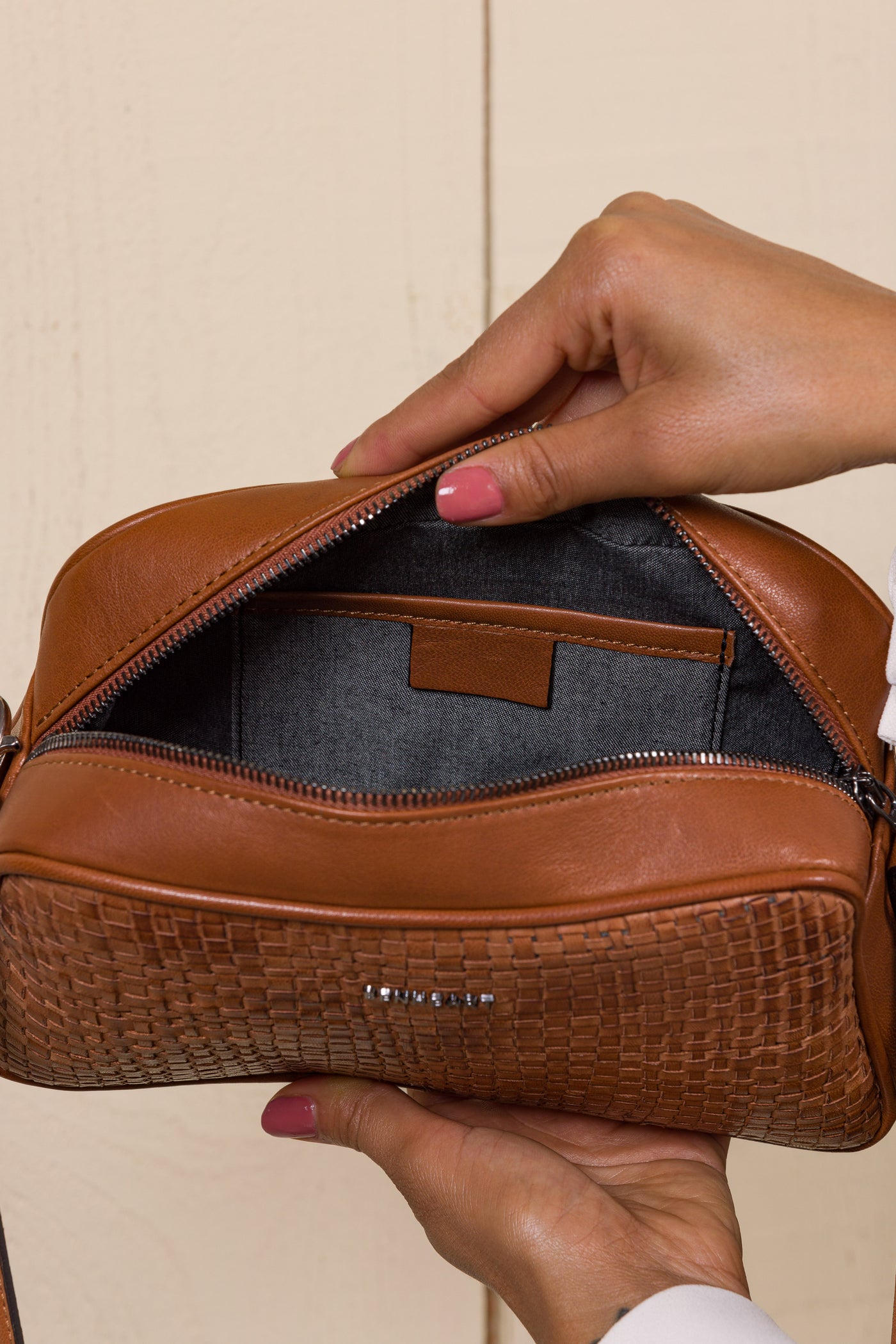 Close-up of the Benheart Afef Medium leather crossbody bag in Cuoio color, held open by a model to showcase interior compartments and detailing.