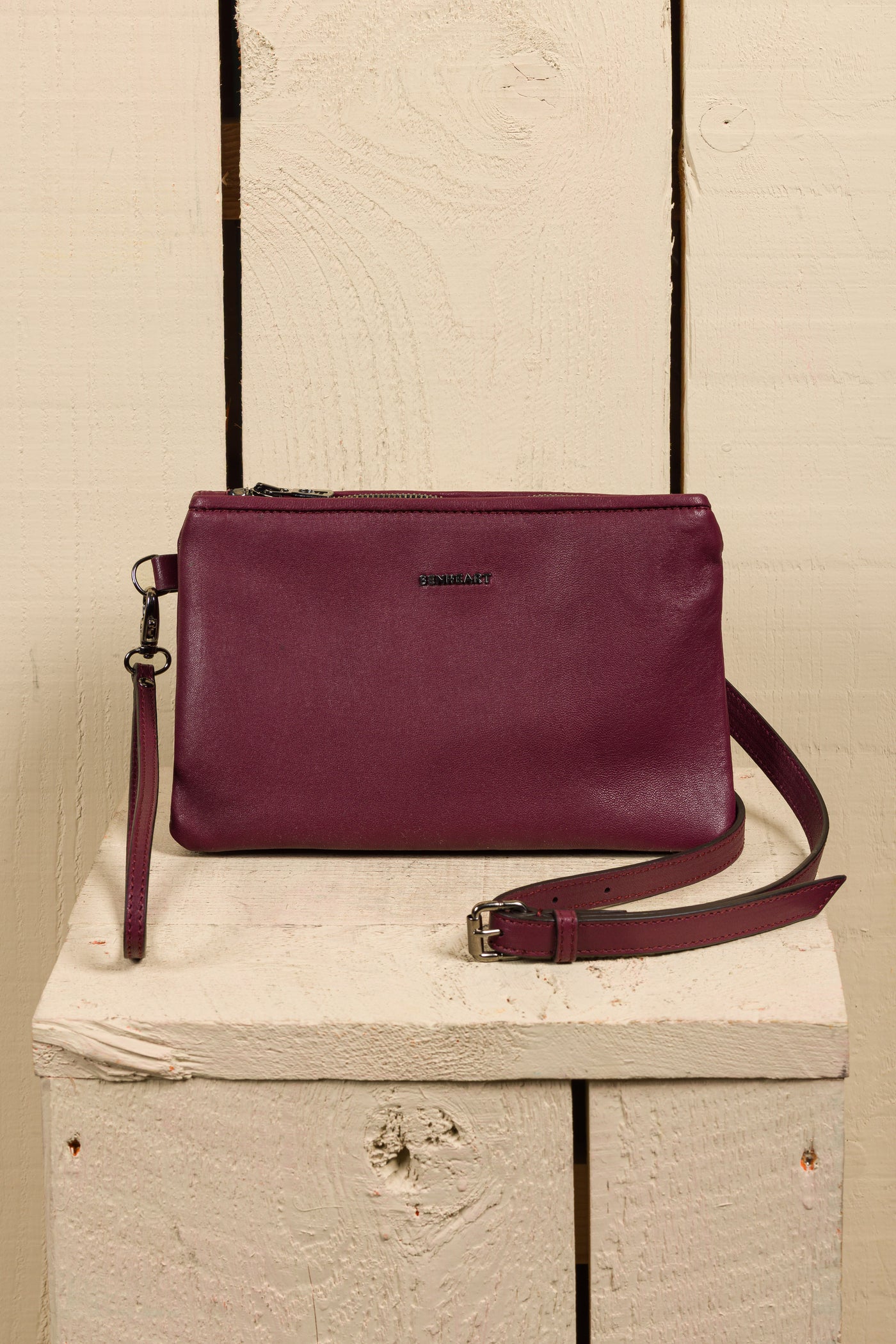 Front view of the Benheart Desert Pochette leather clutch in prugna, highlighting the two zippered compartments and adjustable shoulder strap.