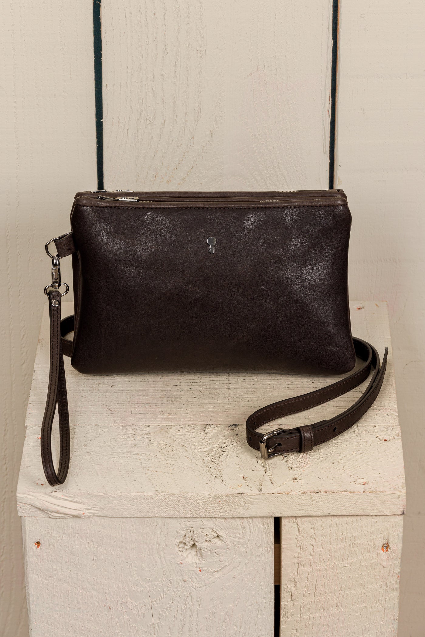 Front view of the Benheart Desert Pochette leather clutch in testa di moro dark brown, highlighting the two zippered compartments and adjustable shoulder strap.