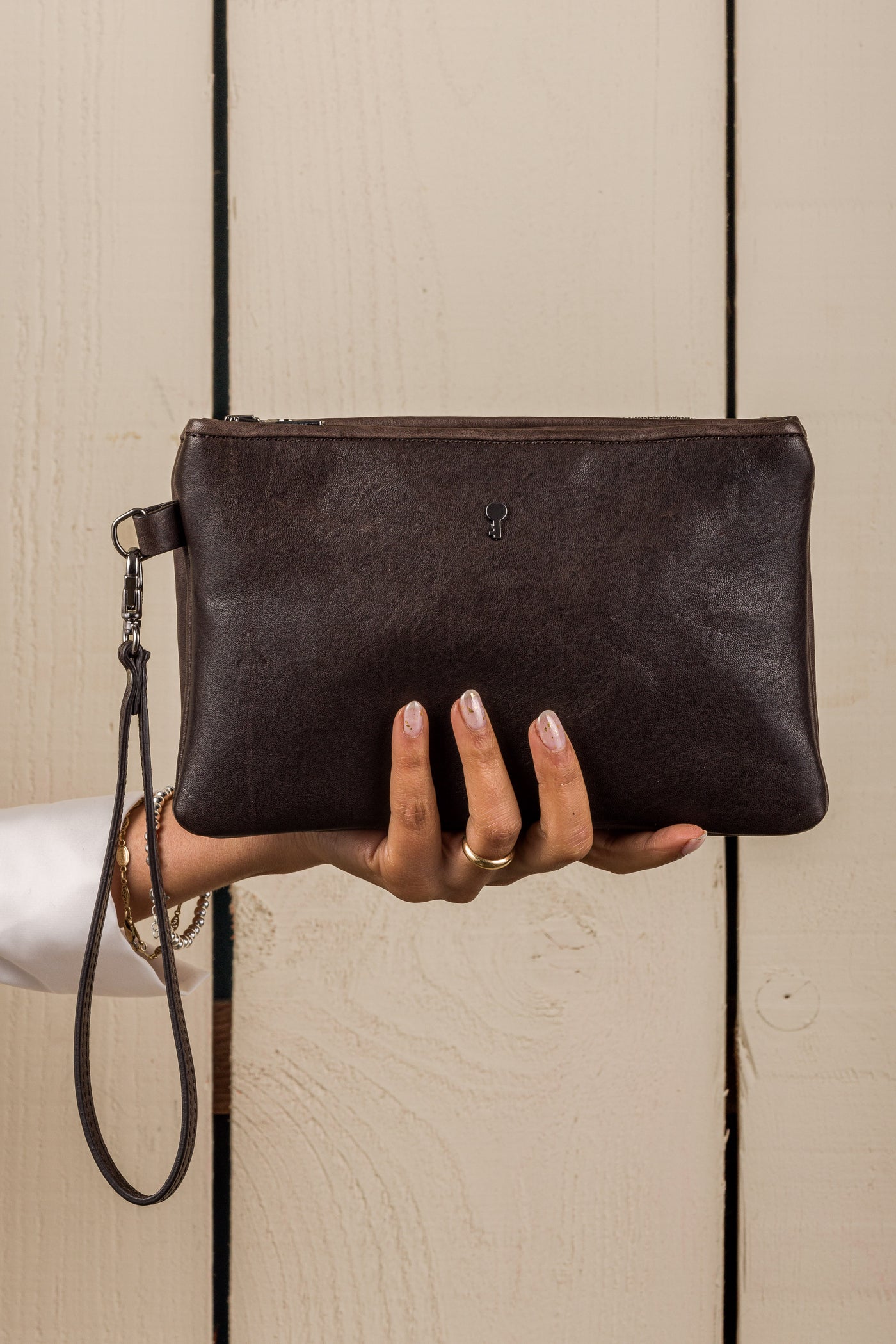 Front view of the Benheart Desert Pochette leather clutch in dark brown held in hand by a model, compact size, handcrafted in Italy.