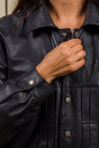 Detail of a model fastening the Jasmine women’s black leather jacket with metal buttons engraved with the Benheart logo.