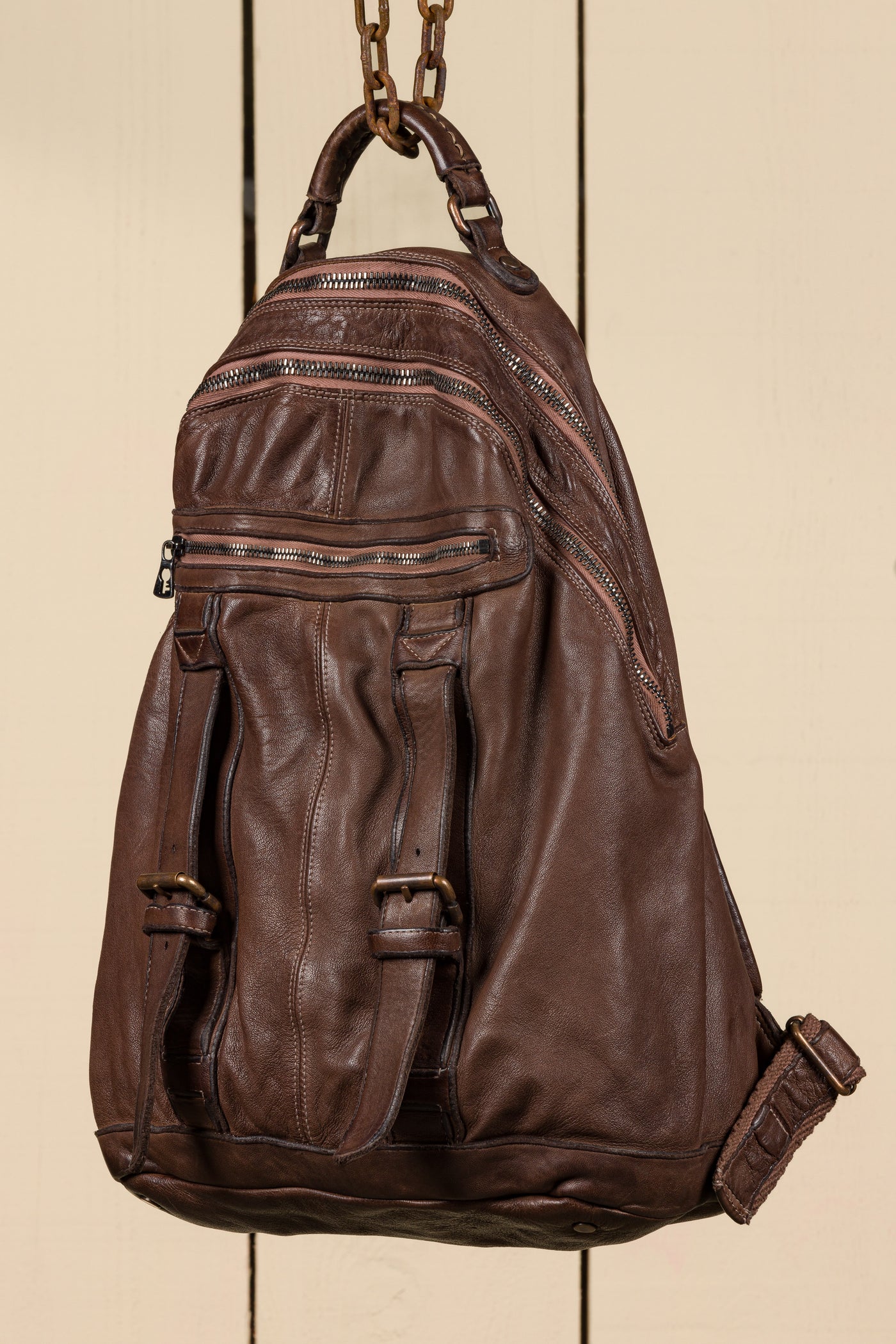 Three-quarter view of the Lorenzo unisex leather backpack in brown, showing front pockets and zipper details.