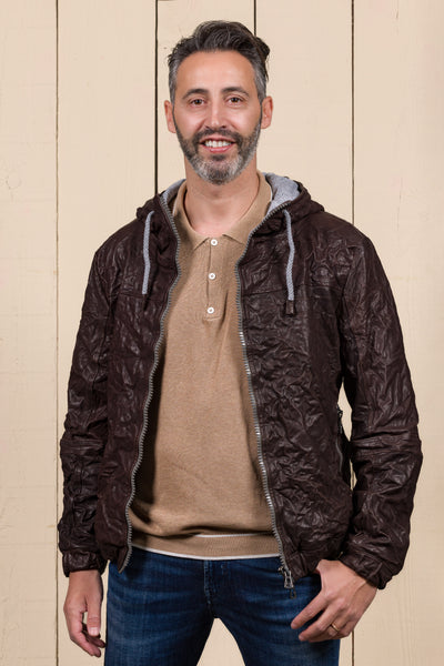 Model wearing a Michelangelo men's leather jacket with hood, in dark brown, handcrafted by Benheart in Florence, Italy, with the jacket open.