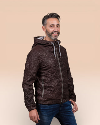 Angled view of a model wearing the Michelangelo men's leather jacket in dark brown, with the collar open, featuring visible zippers and hood drawstrings.