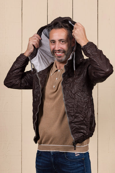 Angled view of the model wearing the Michelangelo men's leather jacket in dark brown, shown with the jacket open while adjusting the hood.