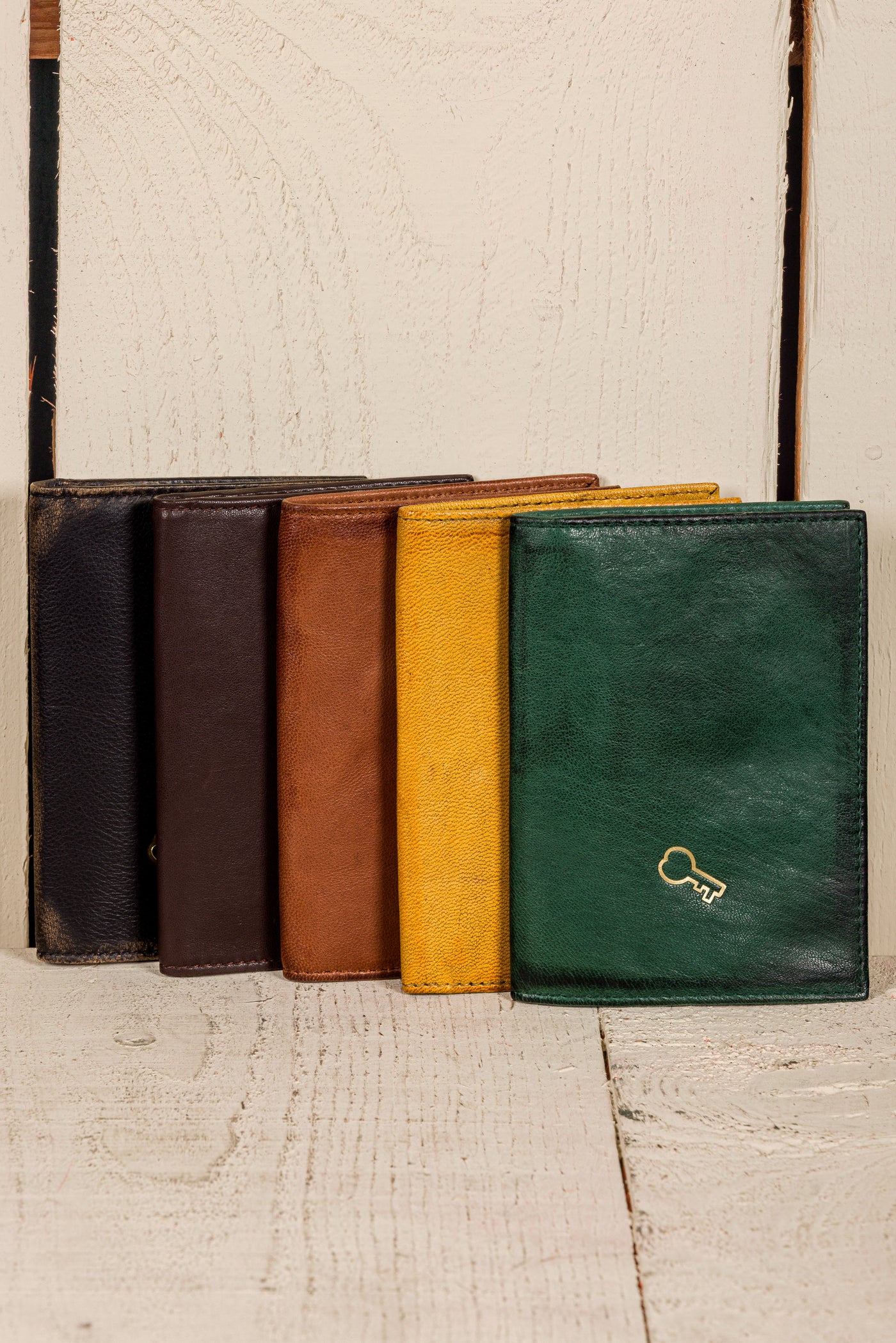 Closed New York leather wallets by Benheart, shown vertically in black, dark brown, tan, yellow, and green with metal key logo
