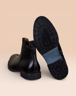 Rear view of Suso black leather Chelsea boots, one turned to show Vibram soles.