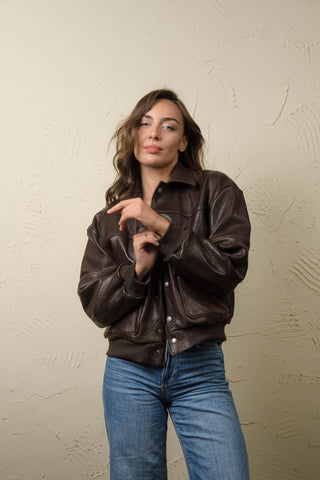 Woman wearing the Hajar dark brown leather bomber jacket, front view, touching the ribbed knit cuff