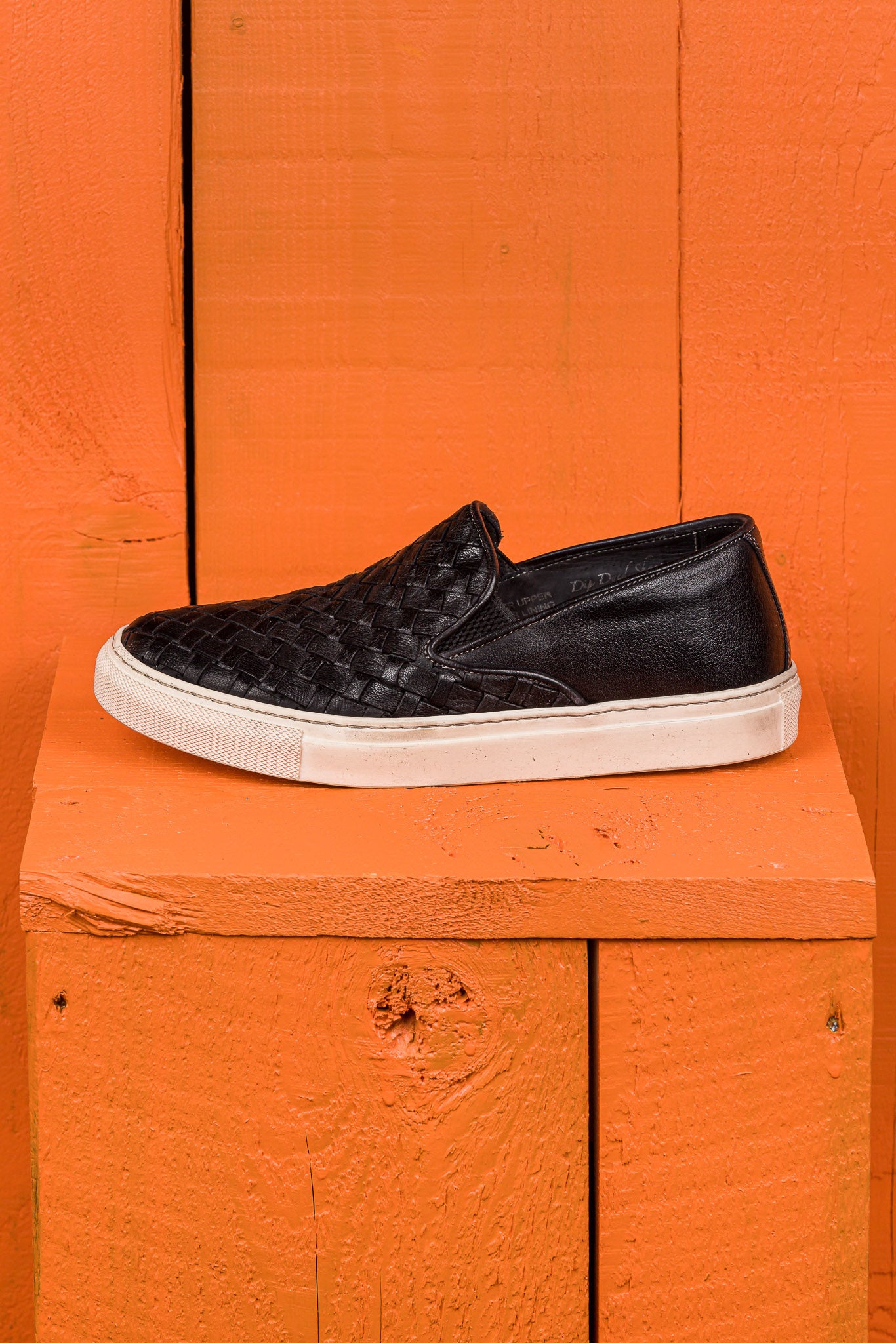 Side view of Iris unisex woven slip-on shoes in black leather with white rubber soles.